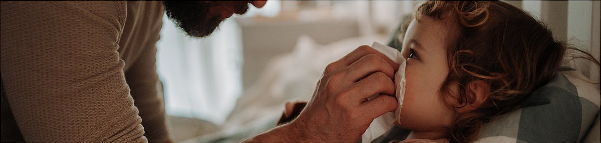 Ein Vater hilft seiner Tochter, die im Bett liegt, die Nase zu putzen und hält das Taschentuch an Ihre Nase