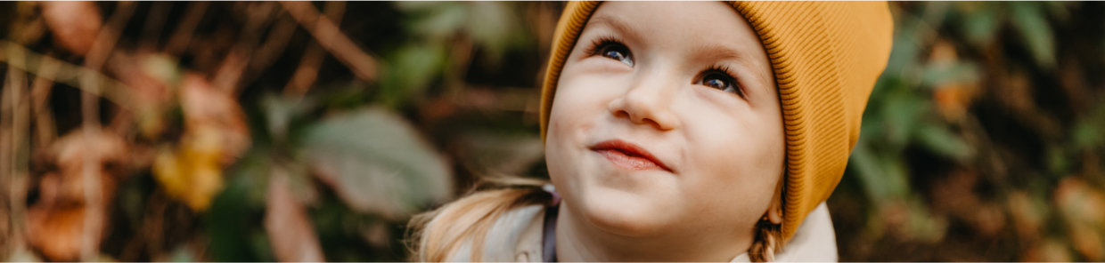 Headerbild – Fröhliches Kind mit gelber Mütze blickt nach oben – Symbolbild für Nasennebenhöhlenentzündung bei Kindern