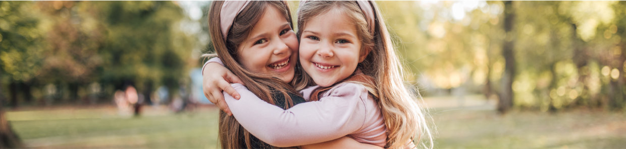 Zwei Mädchen stehen im Park und umarmen sich lachend.