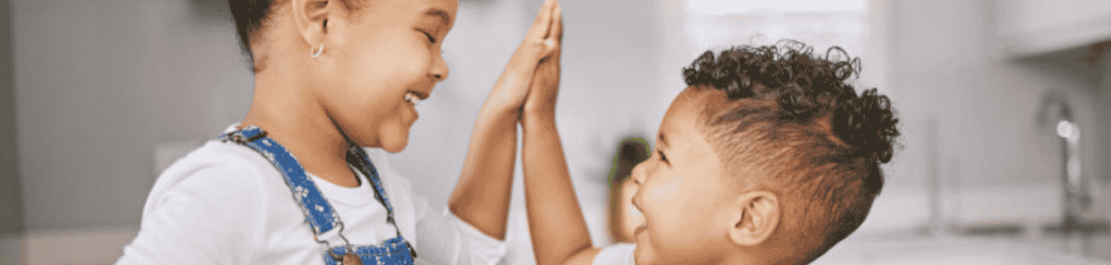 Zwei Kinder lachen und geben sich ein High-Five in einer Küche.