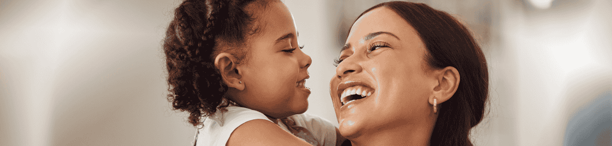 Headerbild – Kind umarmt Mutter von hinten, beide lachen – Symbolbild für was tun bei Mittelohrentzündung bei Kindern